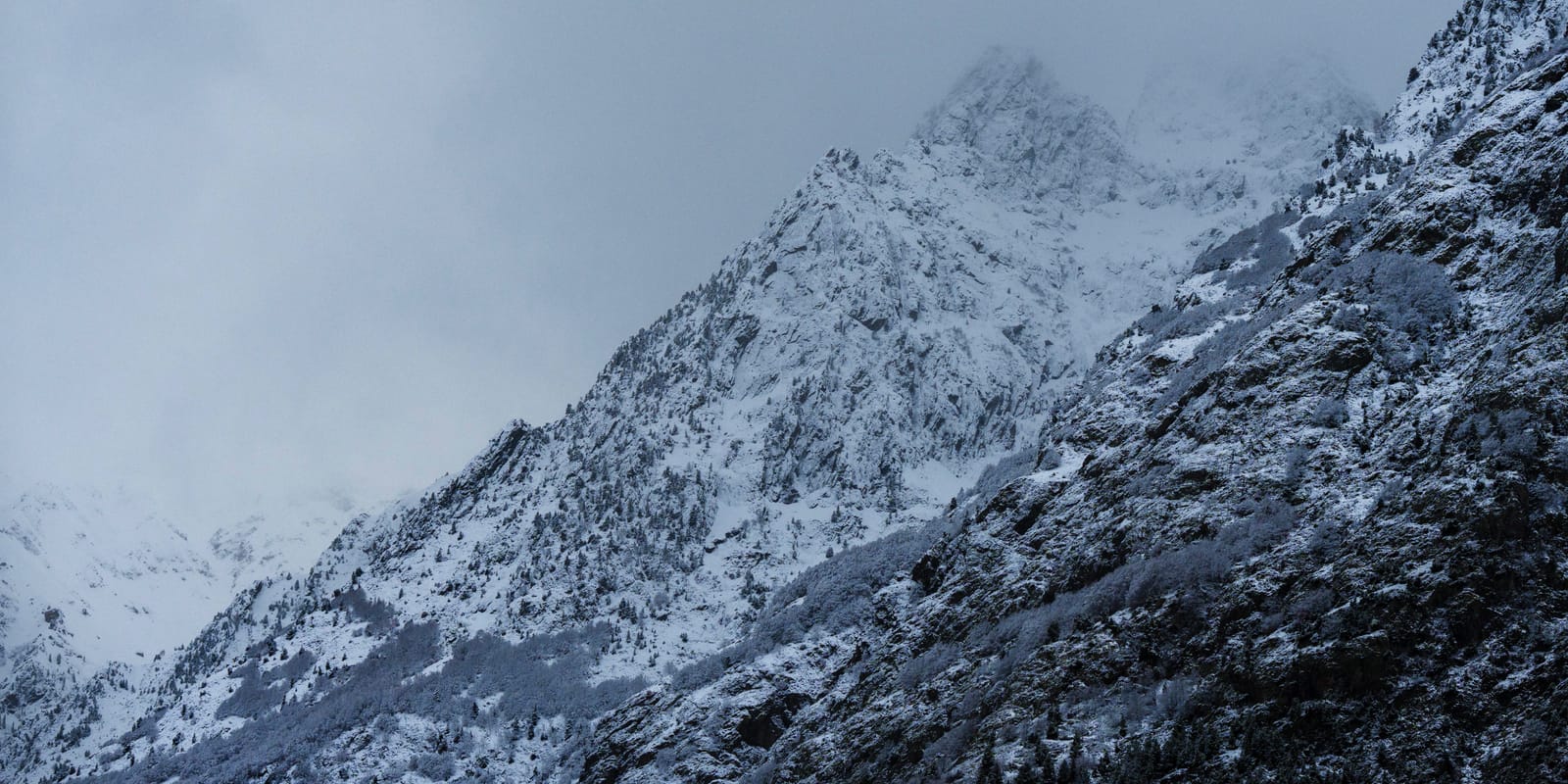 Snow-covered mountain slopes under low cloud, dimly lit.